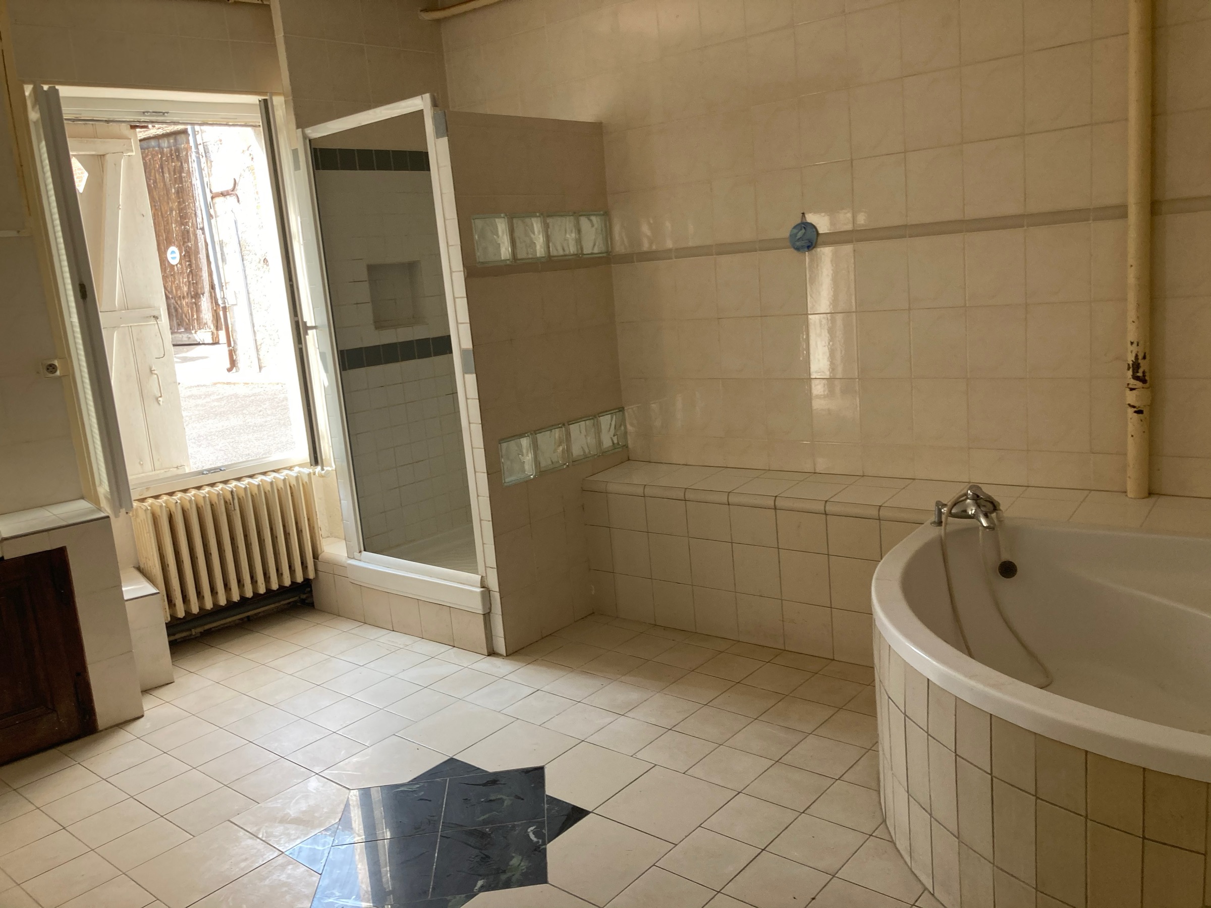 Ancienne salle de bain vétuste avec carrelage beige et baignoire d'angle