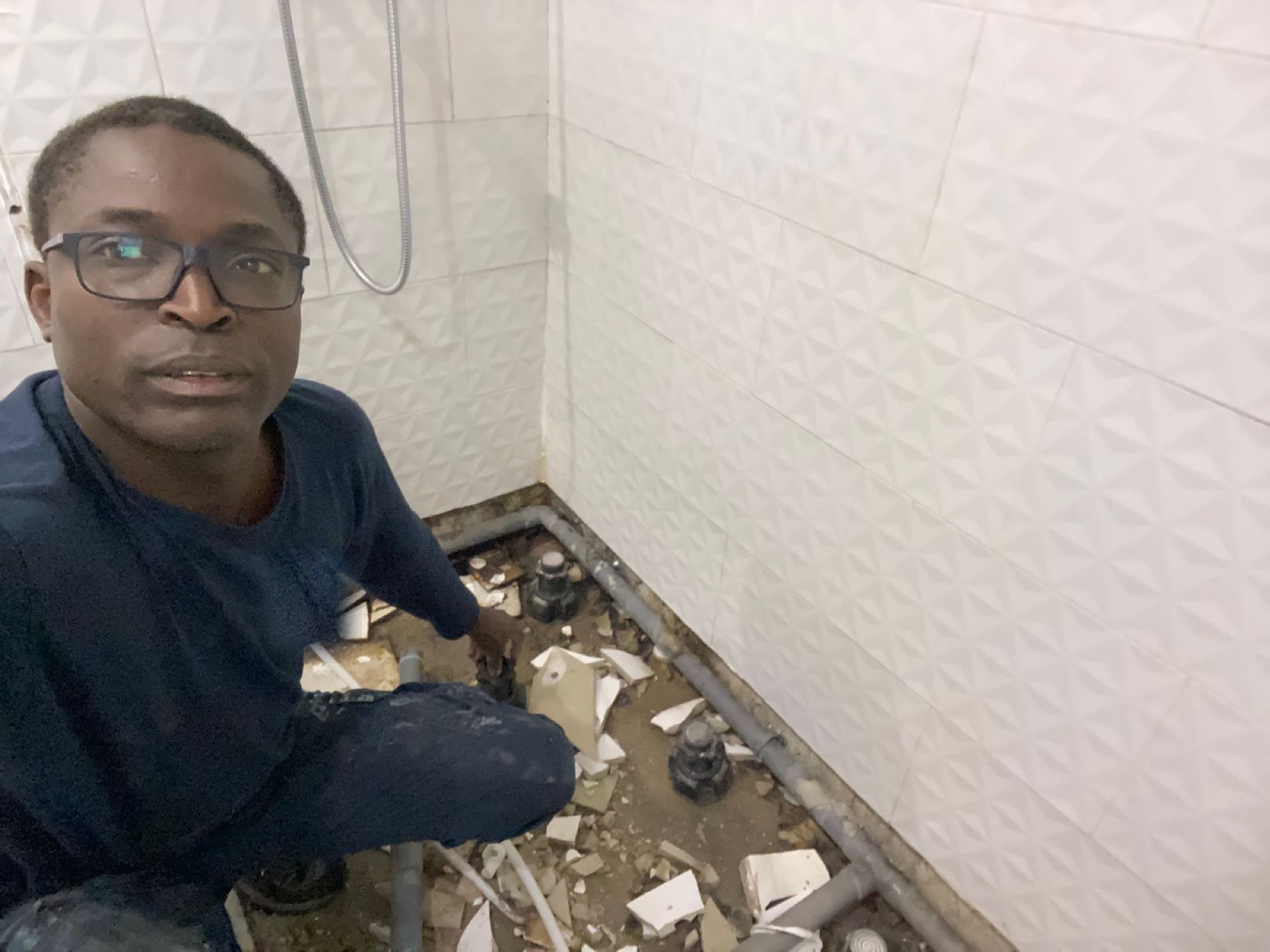 Christian Niangouna agenouillé sur un chantier de salle d'eau, dépose du carrelage et reprise des évacuations